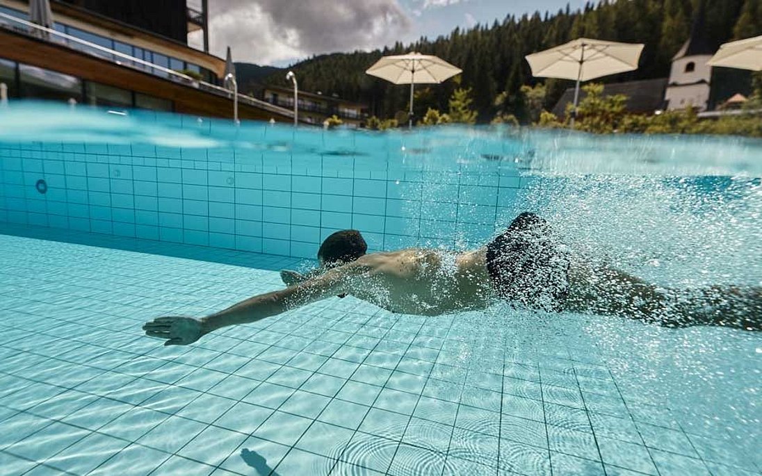 Unterwasseraufnahme eines Mannes der im klaren Hotelaußenpool schwimmt