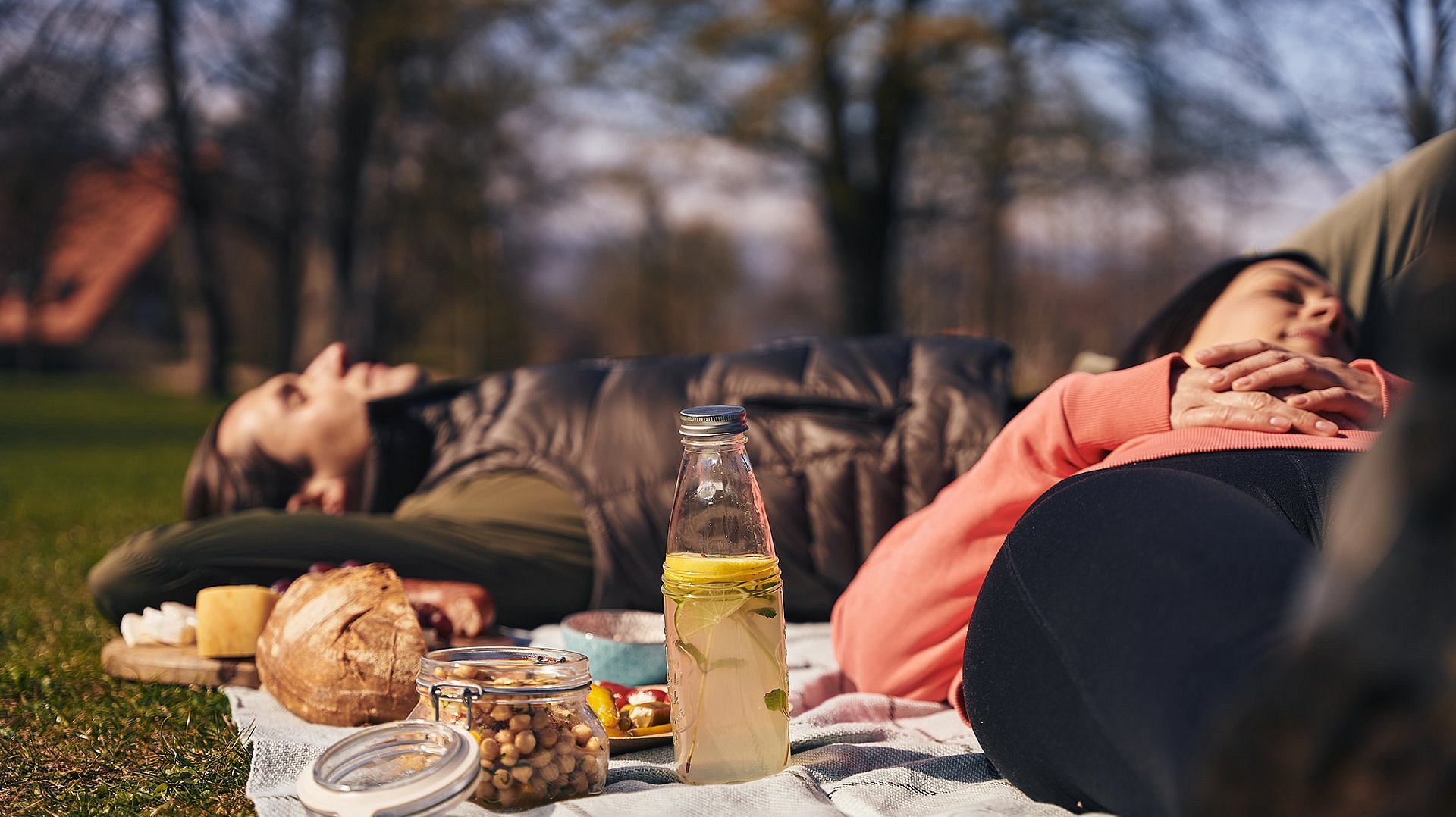 Couple enjoys the autumn weather and lies on meadow with picnic blanket and provisions and sleeps
