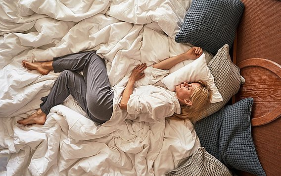 Blonde Frau liegt im kuscheligen Hotelbett mit vielen Kissen und schläft
